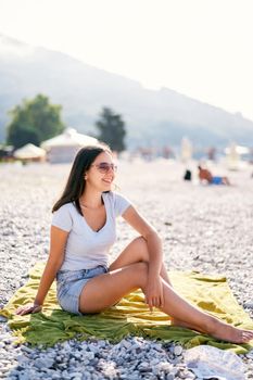 Young smiling woman sits on a blanket on the beach. High quality photo