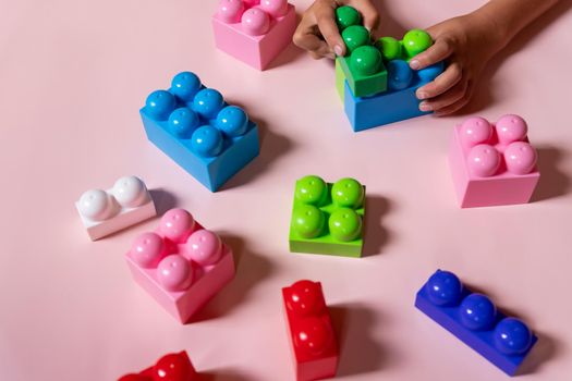 Top view on child's hands playing with colorful wooden bricks on the white table background.Kid building with geometric shapes.