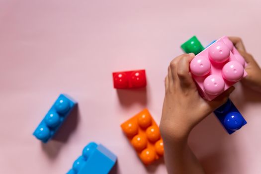 Top view on child's hands playing with colorful wooden bricks on the white table background.Kid building with geometric shapes.