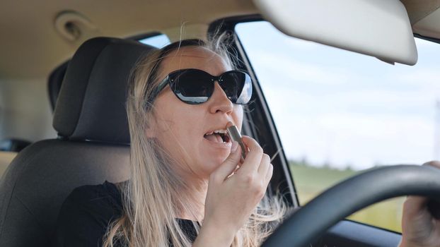 A woman paints her lips while driving