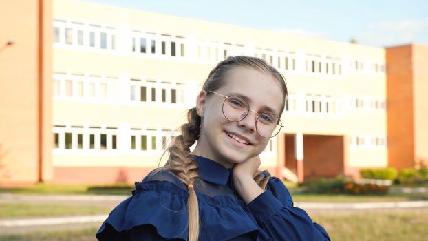 A teenage girl wearing glasses in front of a school