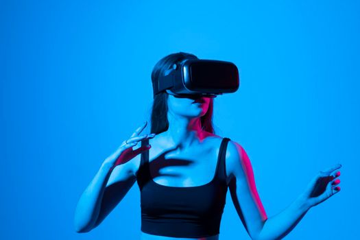 Young brunette woman wearing virtual reality device, vr glasses and playing a game with a friends online in neon light