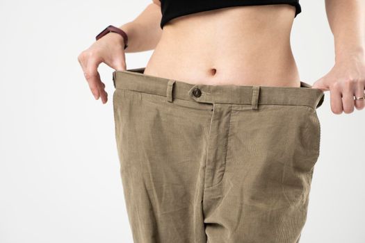 Slim sporty woman in beige pants showing a result of weight loss on white background. Diet concept and weight loss