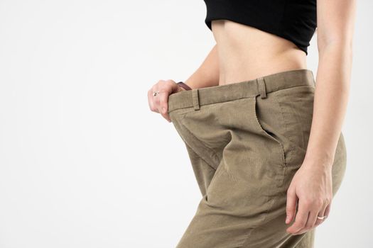 Side view of woman in beige oversize pants showing a result of weight loss on white background. Diet concept and weight loss