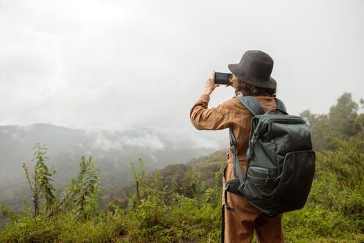 Back view of woman holding backpack and making photo of mountains during travel in Africa