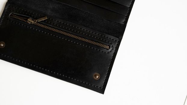 Details of man's handmade wallet on a white surface. Wallet made of genuine black leather with a slots for cards and big zip pocket on a white background. Accessories for men