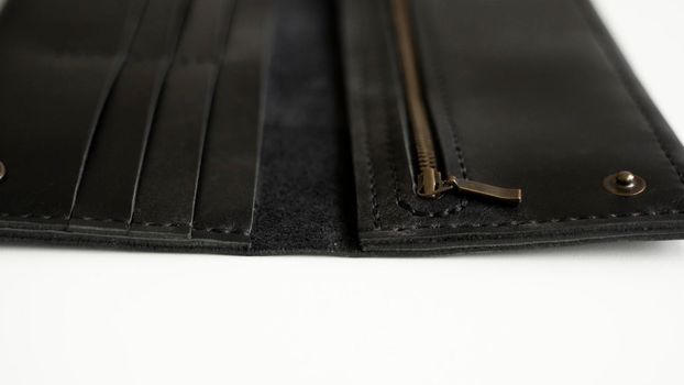 Details of man's handmade wallet on a white surface. Wallet made of genuine black leather with a slots for cards and big zip pocket on a white background. Accessories for men