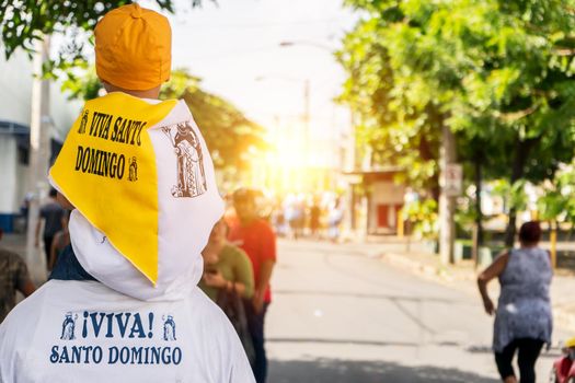 Unrecognizable man from behind carrying his grandson on his shoulders during the celebration of the traditional festivities in honor of Santo Domingo de Guzman, in Managua, Nicaragua