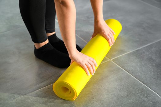 Girl is preparing to unwrap yellow roll of sports mat for fitness. Hands are lying on mat, close-up. Concept of healthy lifestyle.