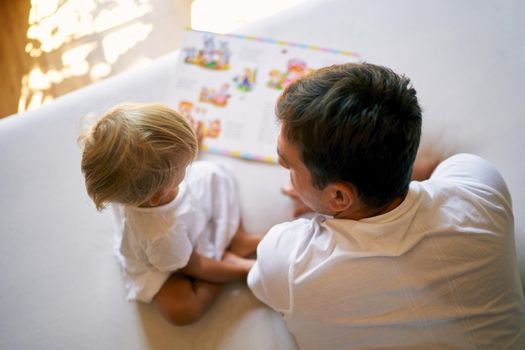Dad reading a book to a little girl pointing his finger. High quality photo