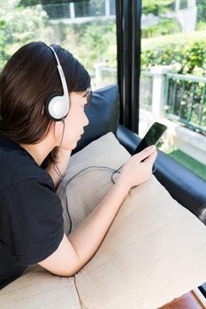 Young girl with headphones and listening to music from mobile phone on the sofa in living room at home