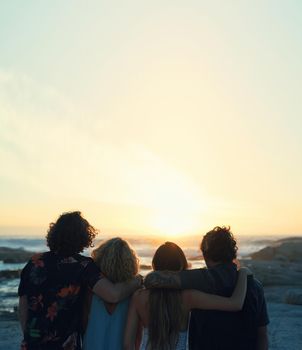 group of friends embrace on beach looking at beautiful sunset enjoying summer vacation lifestyle.