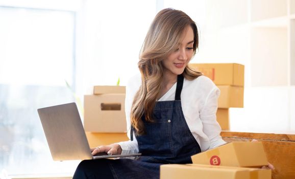 Portrait, entrepreneur, young Asian woman, freelance business, sme business, online shopping, working on laptop computer with parcel box on home office table, online business and delivery concept..