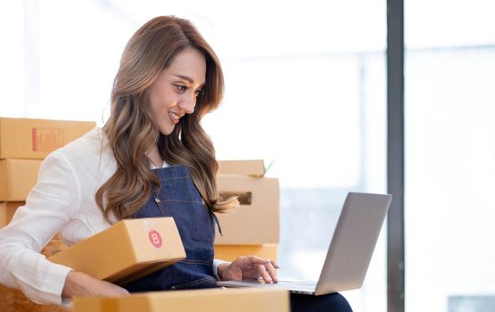 Portrait, entrepreneur, young Asian woman, freelance business, sme business, online shopping, working on laptop computer with parcel box on home office table, online business and delivery concept..