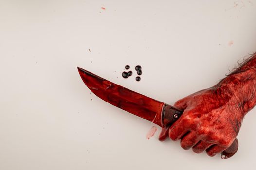 A man with bloody hands holds a knife on a white background