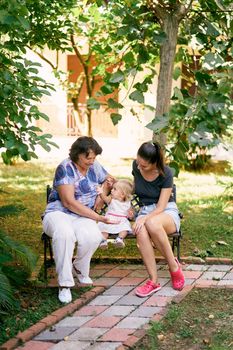 Mom, grandmother and little girl are sitting on a wooden bench in the park. High quality photo