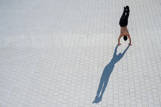 Shirtless man walks on his hands outdoors. View from above