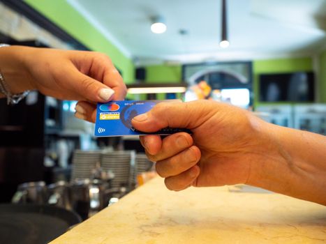Customer paying for their order with a credit card in a cafe. Bartender holding a credit card reader machine and returning the debit card to female customer after payments.