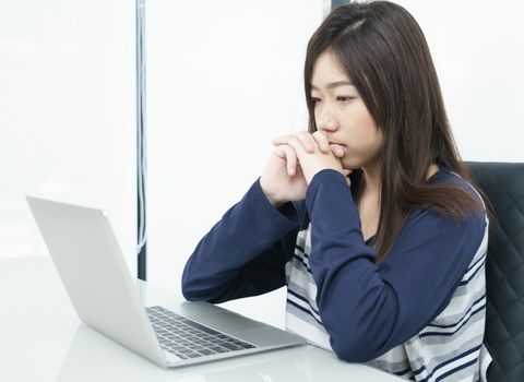 Young female student sitting in living room using laptop at desk learning online