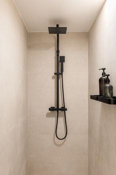 Black shower and ceramic tiled wall. Vertical view of modern minimalist interior of beige color.