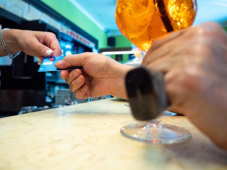 Customer paying for their order with a credit card in a cafe. Bartender holding a credit card reader machine and returning the debit card to female customer after payments.
