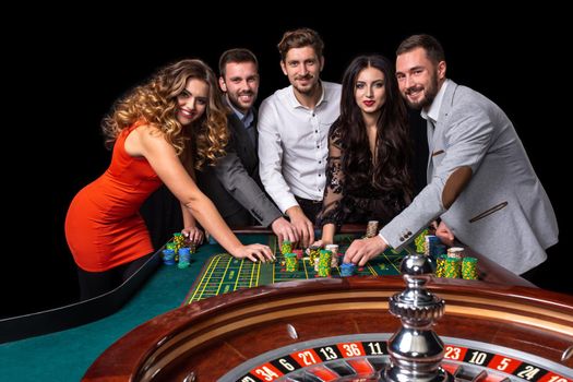 Group of young people behind roulette table in a casino. Black background