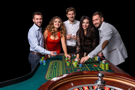Group of young people behind roulette table in a casino. Black background