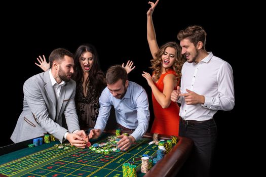 Adult group celebrating friend winning at roulette. Roulette table in a casino. Black background