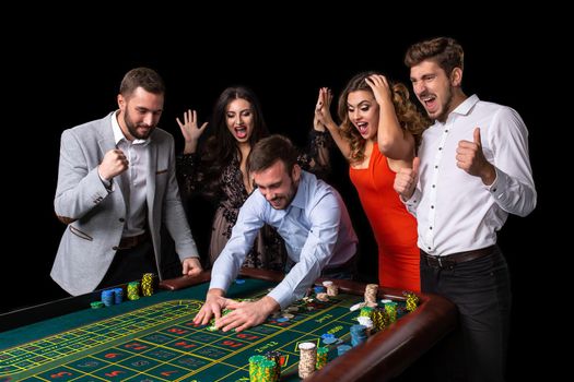 Adult group celebrating friend winning at roulette. Roulette table in a casino. Black background