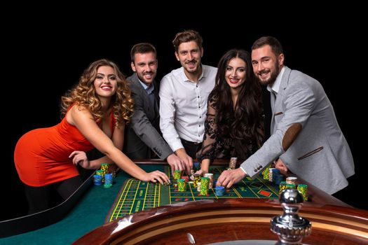 Group of young people behind roulette table in a casino. Black background