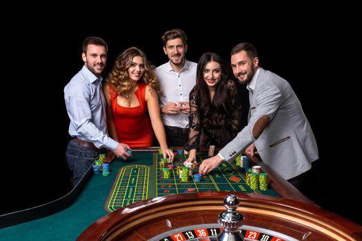 Group of young people behind roulette table in a casino. Black background