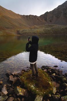 Travel photographer taking pictures of nature on a smartphone, mountain landscape by the lake. Tourist on adventure vacation.