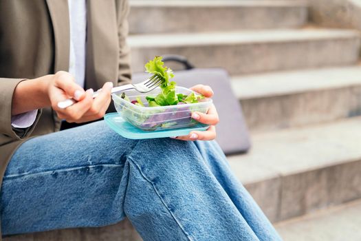 close up of a woman's hands stabbing salad out of the lunch box with a fork, concept of urban lifestyle and healthy food, copy space for text