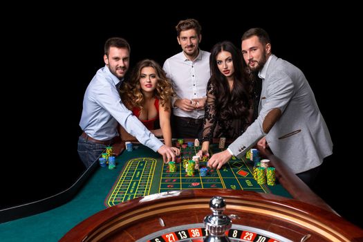 Group of young people behind roulette table in a casino. Black background