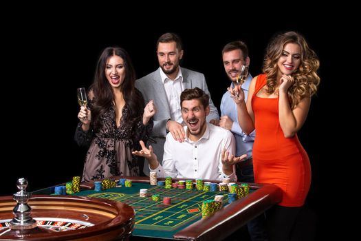 Group of young people looking excited at spinning roulette. Roulette table in a casino. Black background