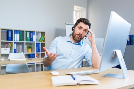 Upset businessman with headset working in office with computer
