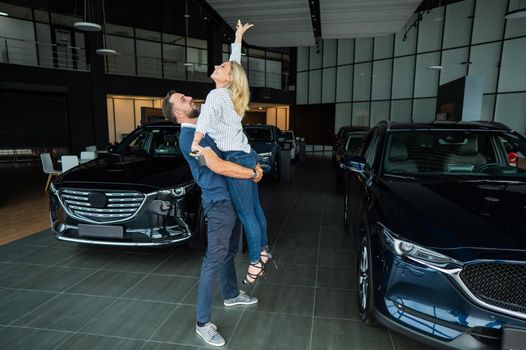 Happy caucasian couple hugging while buying a new car in a car dealership