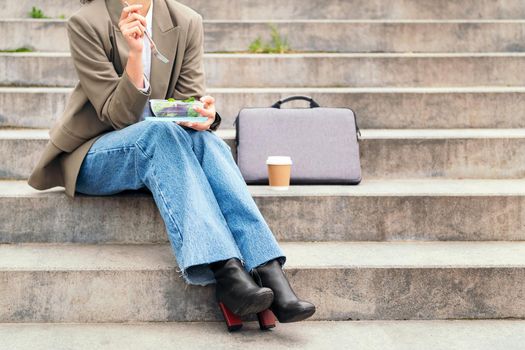 unrecognizable young woman eating a salad from a lunch box sitting on a staircase during a break from work, concept of urban lifestyle and healthy food, copy space for text