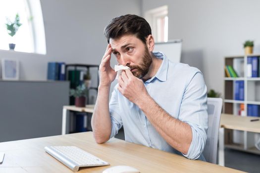 Businessman sick in the office man with allergies sneezes, sitting at a table with a computer