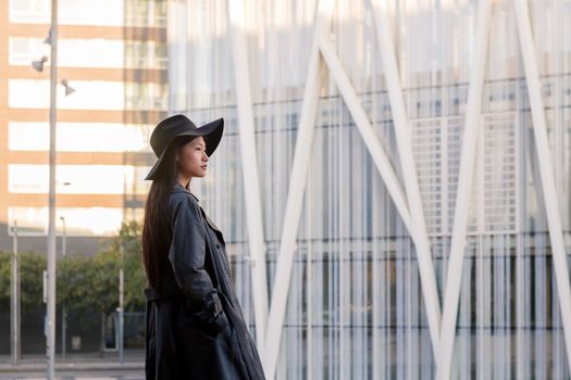 young asian woman in hat and trench coat walking downtown, urban lifestyle concept, copy space for text