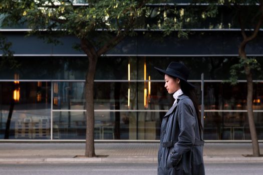 elegant asian woman in hat and trench coat walking in the city, urban lifestyle concept, copy space for text