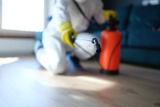 Person in white protective suit in hotel or apartment sprays disinfectant against viruses or rodents. Bedbug disinfection service concept