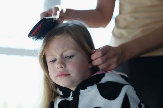 Mother trouble combing unfortunate daughter long hair. Daughter does not allow herself to be combed concept