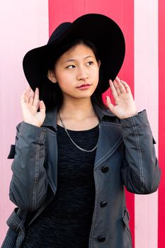 vertical portrait of a young beautiful classy asian girl posing in a pink background, concept of elegance and fashion lifestyle
