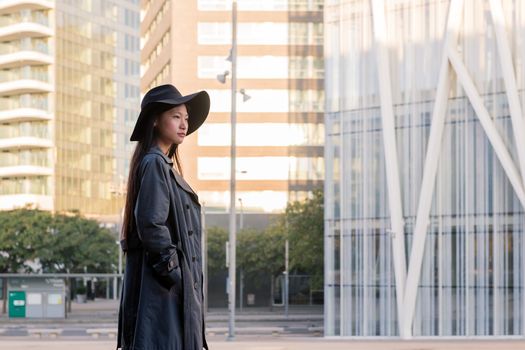 elegant asian woman in hat and trench coat walking downtown, urban lifestyle concept, copy space for text