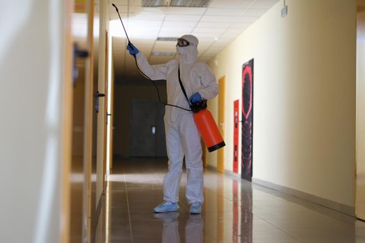 Person in protective suit with disinfectant cleaning public area in during pandemic. Carrying out disinfection and antiviral treatment concept