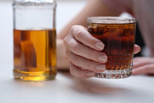 Woman hand holds glass of whiskey or cognac with bottle. Woman suffering from alcohol addiction and depressed woman drinking hard alcohol concept