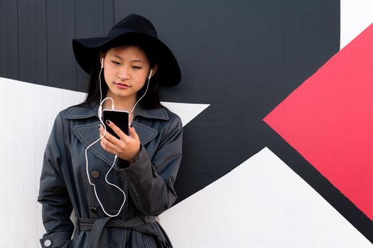 young beautiful classy asian woman with earphones looking at her phone, concept of technology and modern lifestyle, copyspace for text