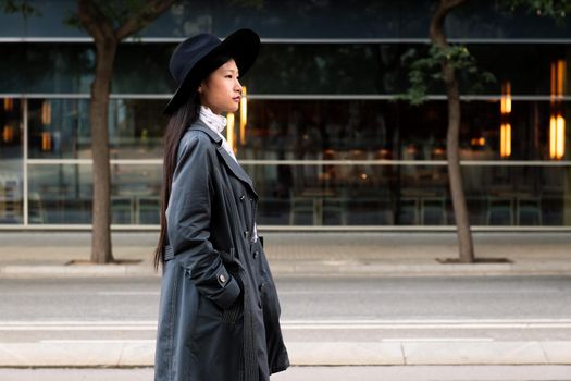 classy asian woman walking in the city with hat and trench coat, concept of elegance and urban lifestyle, copy space for text