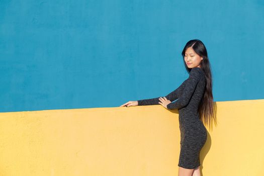 beautiful asian woman posing in a tight dress on a colorful yellow and blue background, concept of fashion and lifestyle, copyspace for text